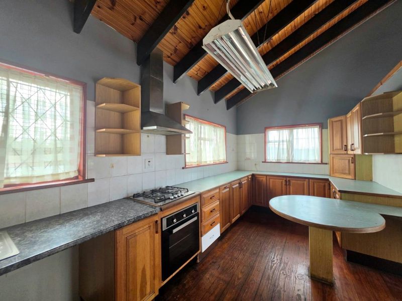 Spacious kitchen featuring timber cabinetry, exposed ceiling beams, gas hob, and built-in oven, offering a functional layout with potential for modern updates.