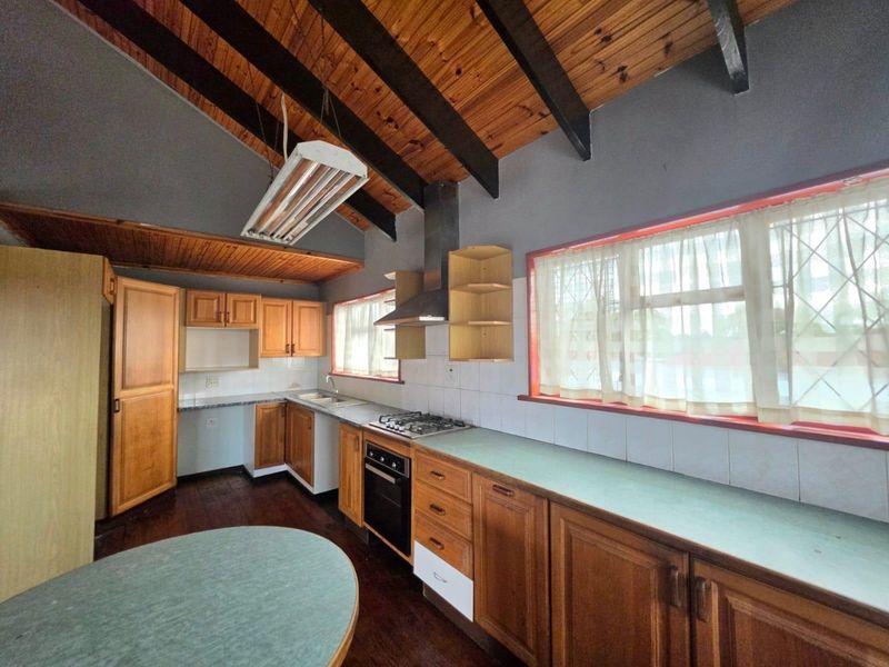 A functional kitchen featuring wooden cabinetry, laminate countertops, built-in oven, gas hob, and exposed timber ceiling beams with a tiled splashback.