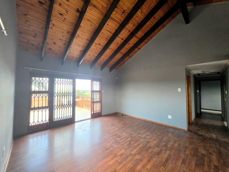 Spacious living area featuring high exposed timber rafter ceilings, laminate flooring, and sliding glass doors leading to an outdoor space.
