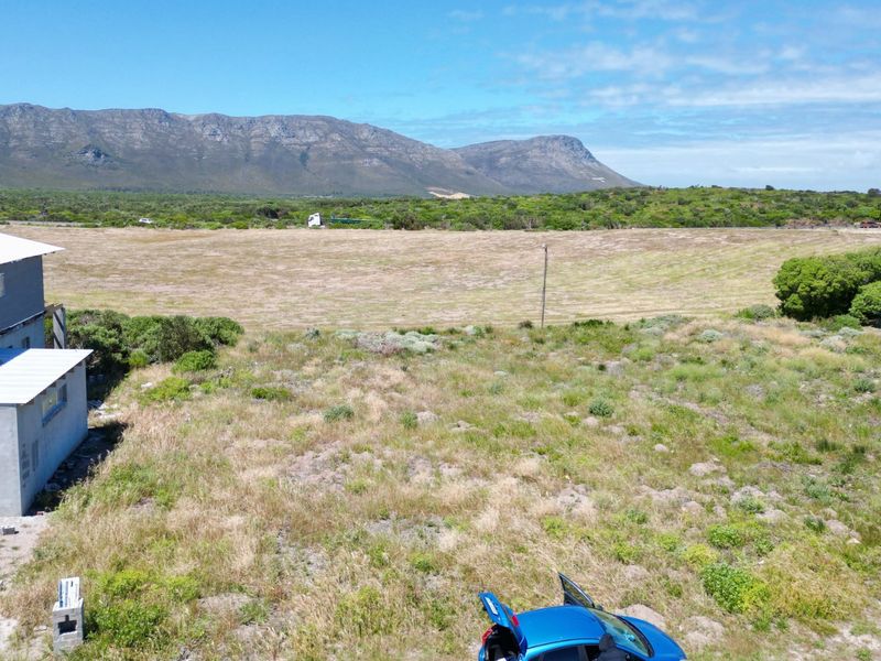 An aerial view of a vacant residential plot featuring natural vegetation and mountain views in the background.
