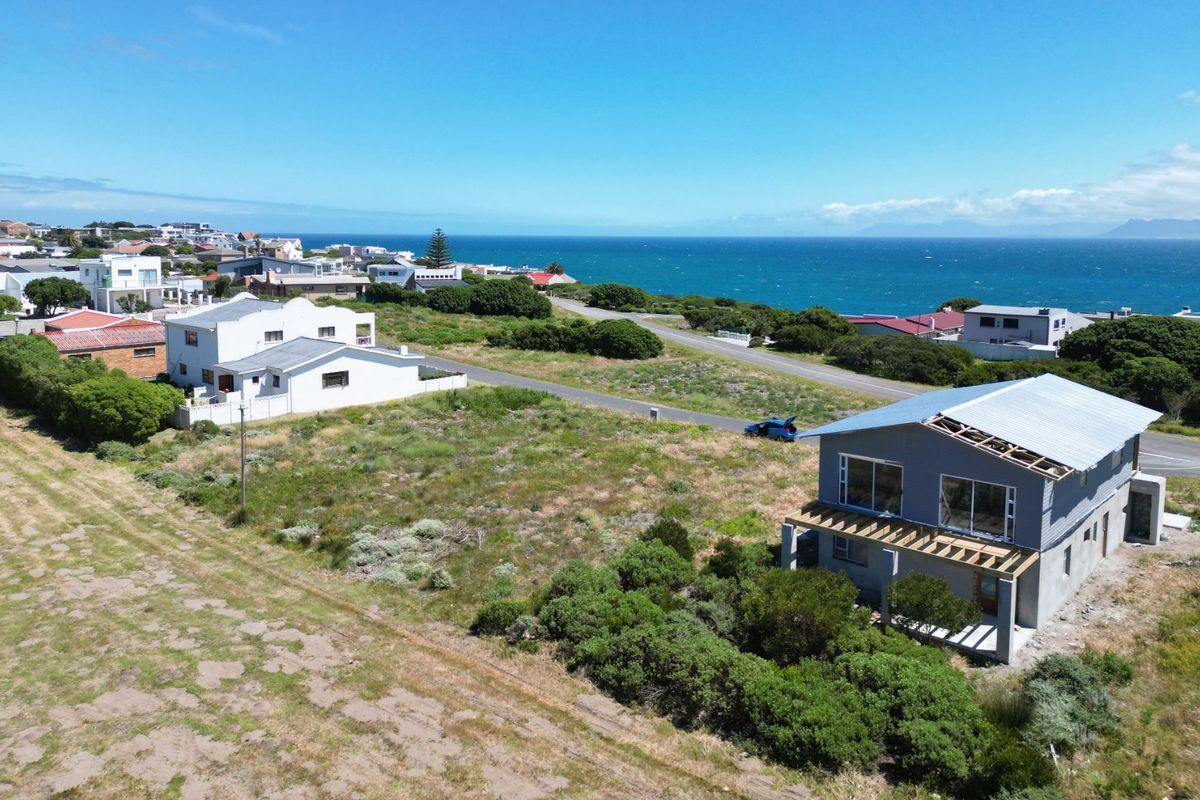 Aerial view of a vacant residential plot featuring coastal views and a partially constructed dwelling with an incomplete roof structure.