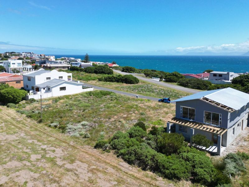 Aerial view of a vacant residential plot featuring coastal views and a partially constructed dwelling with an incomplete roof structure.