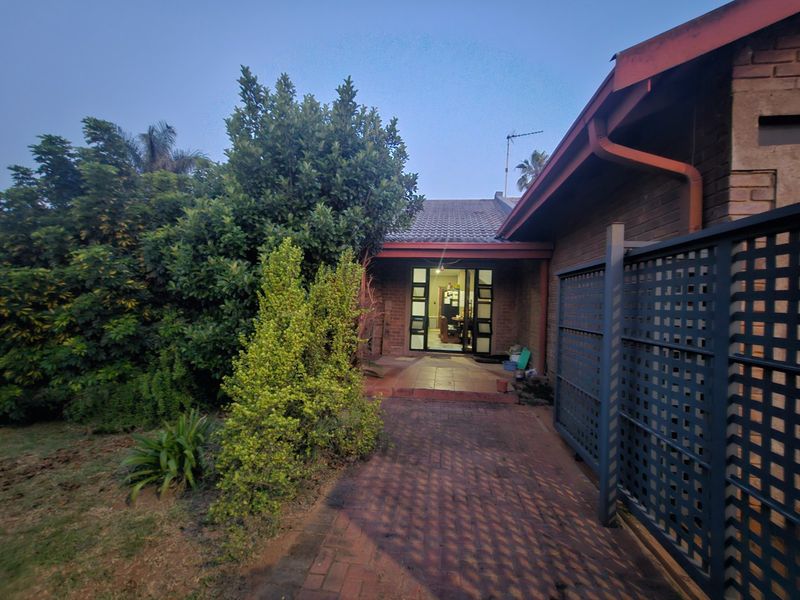 Front entrance view of a brick house featuring a paved walkway, covered porch, and established garden landscaping.
