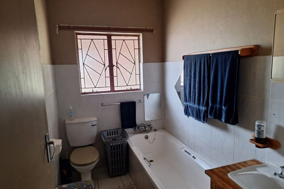 A functional bathroom featuring a bathtub, toilet, and vanity basin with tiled splashbacks and security bars on the window.