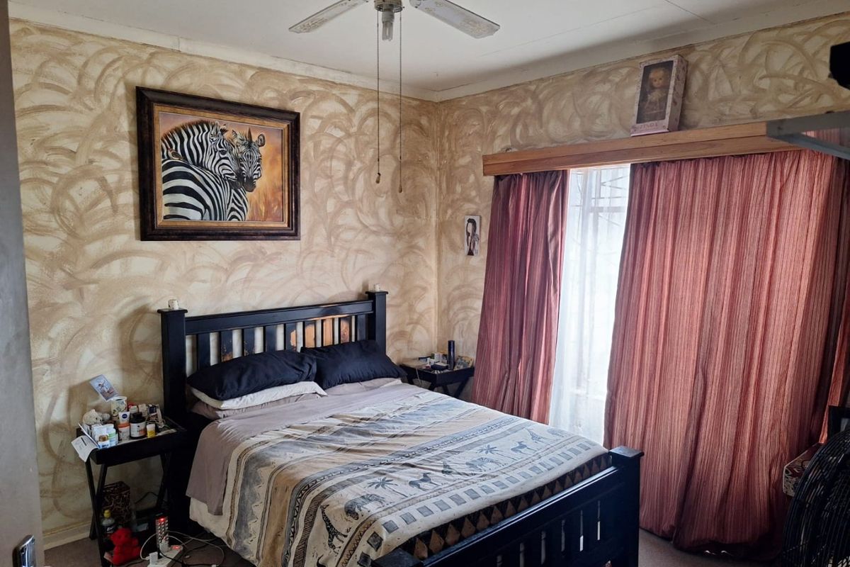 A bedroom featuring a ceiling fan and large window with curtain rails, currently finished with a textured wall treatment.