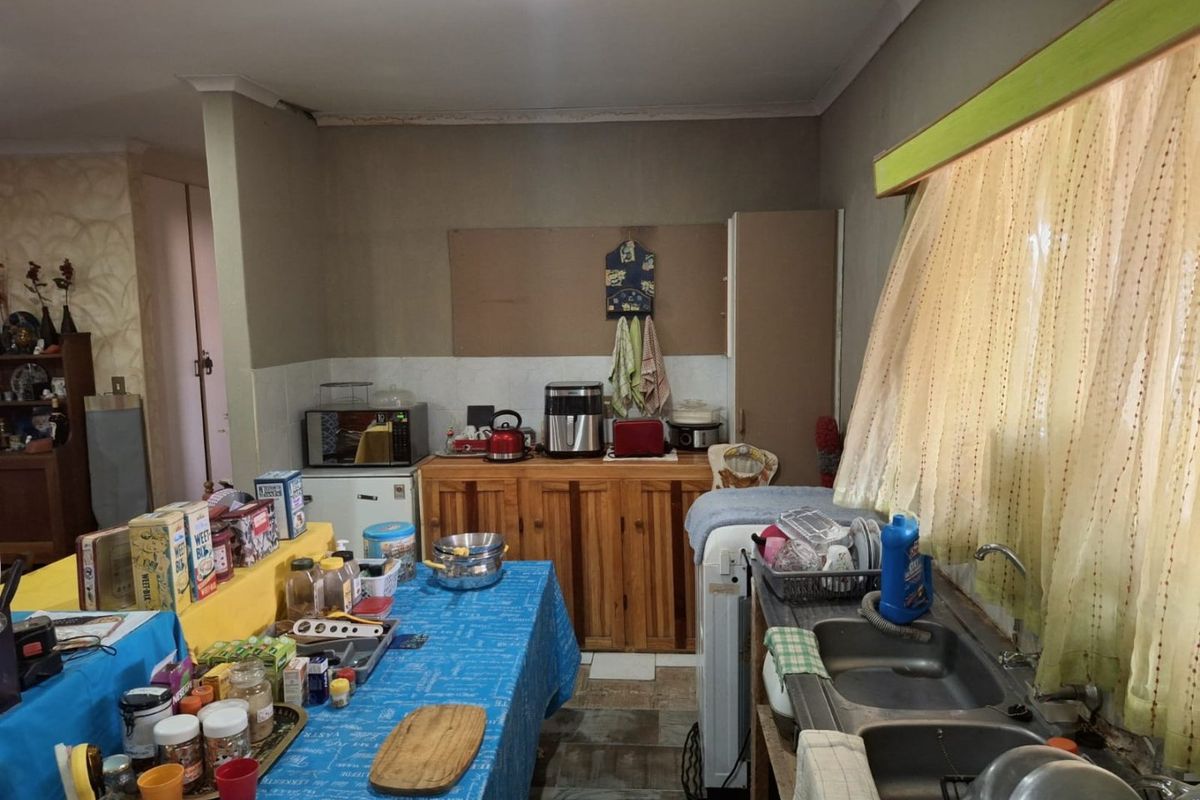 A functional kitchen featuring wooden cabinetry, a double bowl sink, and tiled splashbacks, offering potential for modernization and layout optimization.