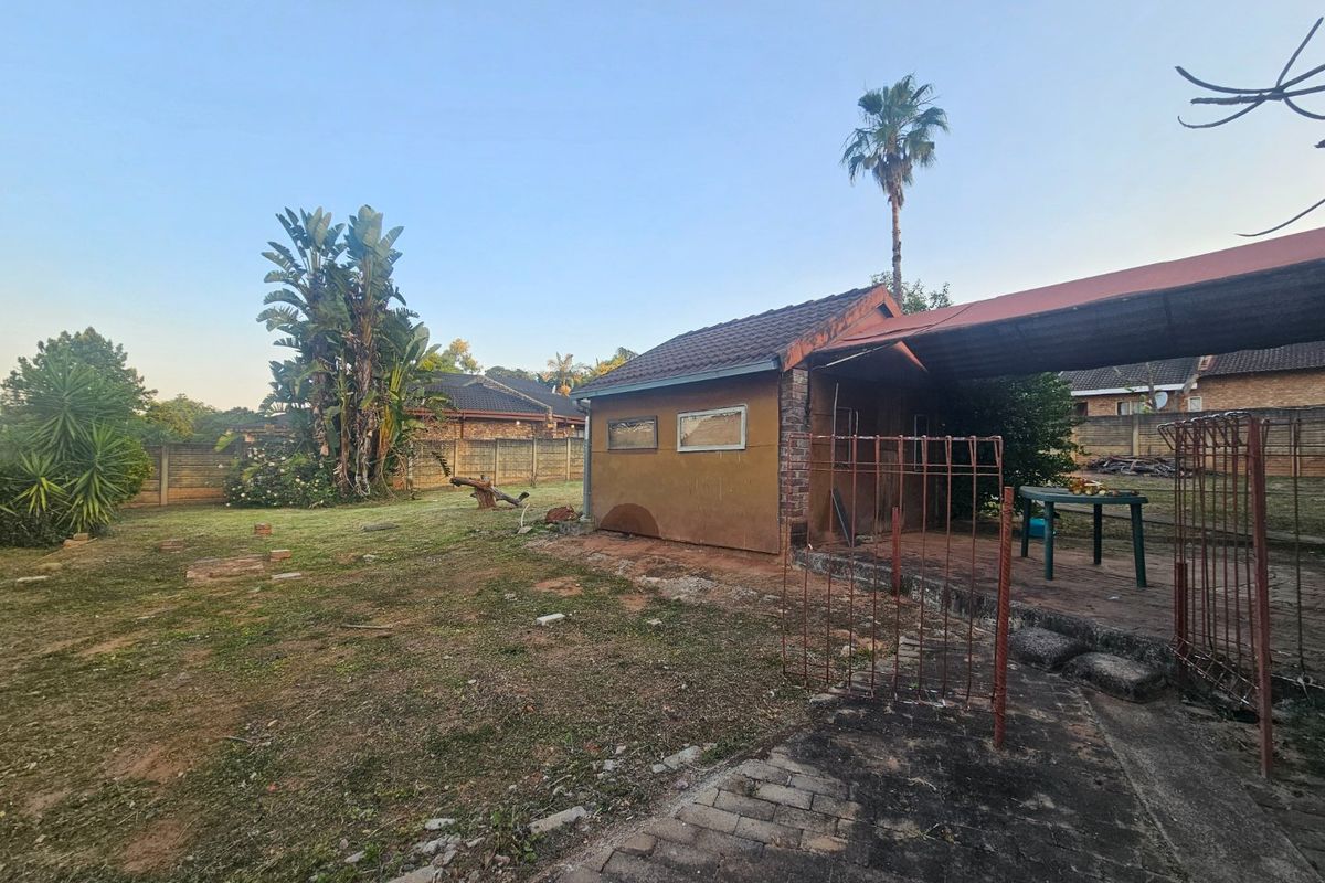 Rear exterior view of the property featuring a garden area, paved section, and a carport structure with a tiled roof.