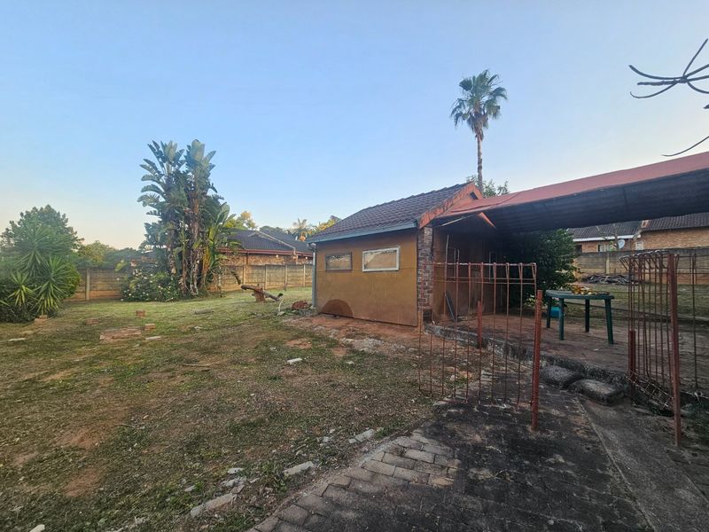 Rear exterior view of the property featuring a garden area, paved section, and a carport structure with a tiled roof.