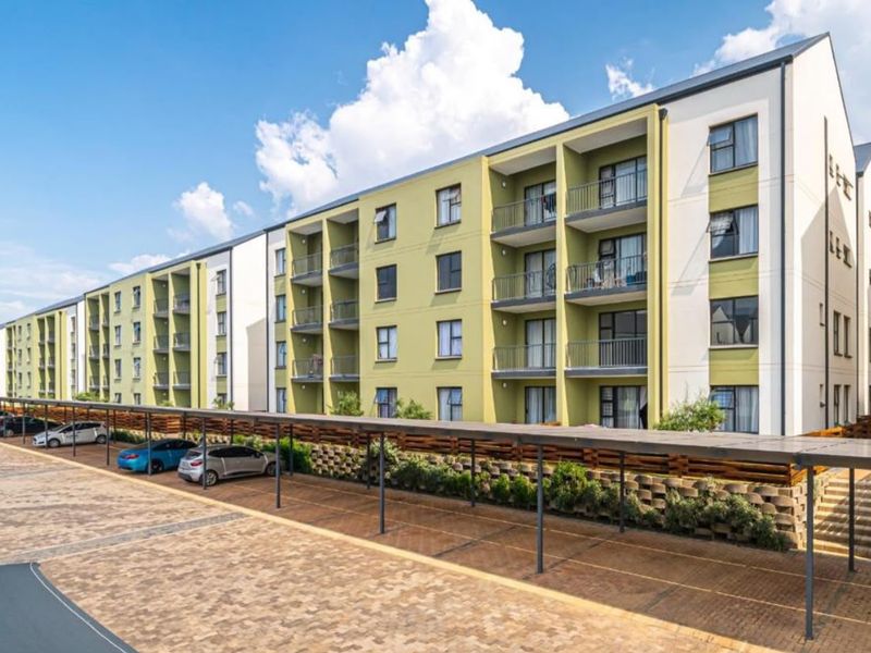 Exterior view of a modern apartment complex featuring multi-story residential units with private balconies and an extensive covered parking area.
