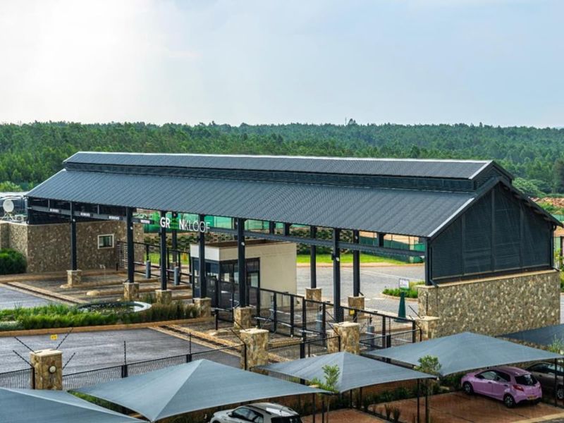 An elevated view of the modern security entrance gatehouse featuring stone cladding, a large metal roof structure, and adjacent shade cloth parking bays.