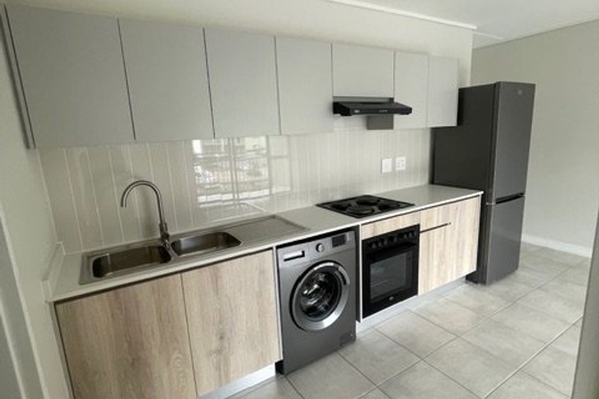 Modern kitchen featuring light wood-tone lower cabinets, grey upper cabinetry, tiled backsplash, built-in oven, hob, extractor fan, and integrated washing machine.
