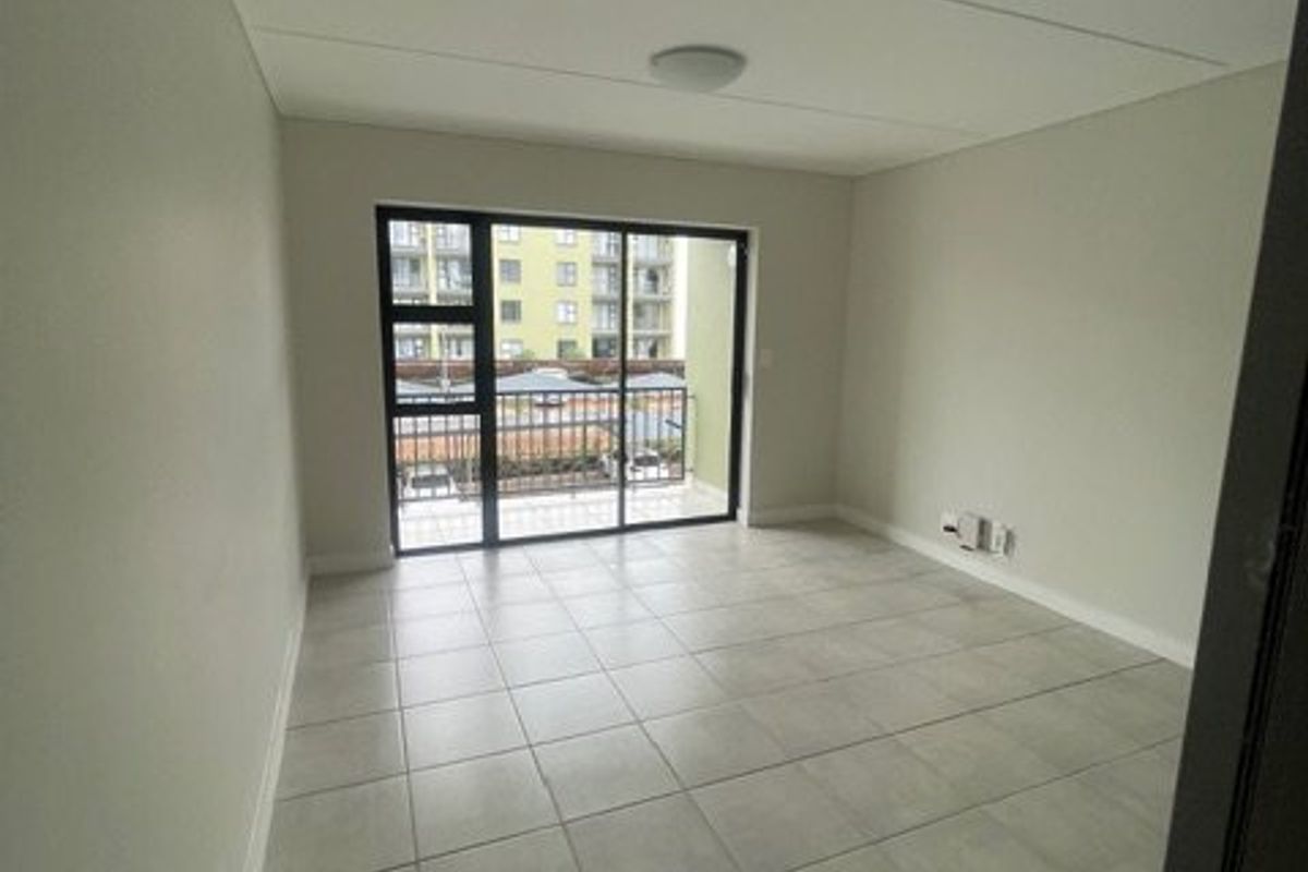 A bright, empty living area featuring neutral tiled flooring and a large sliding glass door providing access to a private balcony.