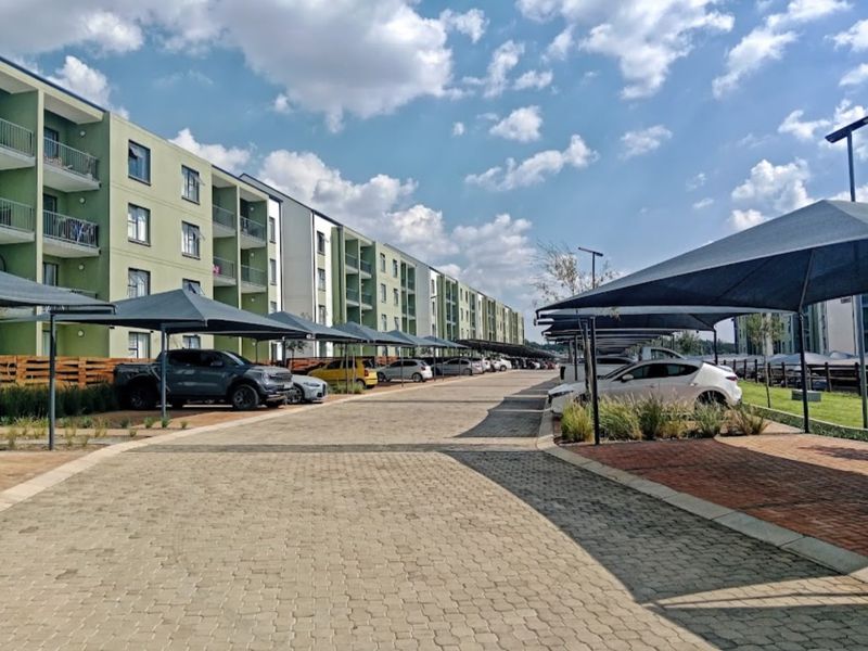 Exterior view of a modern apartment complex featuring paved parking areas with shade cloth carports and multi-story residential units with balconies.