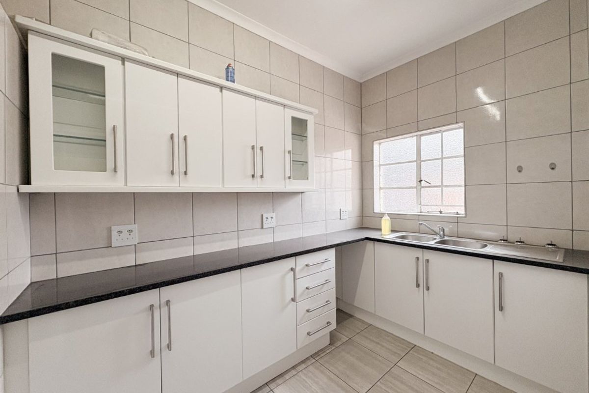 A clean, functional kitchen featuring white built-in cabinetry, dark laminate countertops, a double basin sink, and full-height wall tiling.