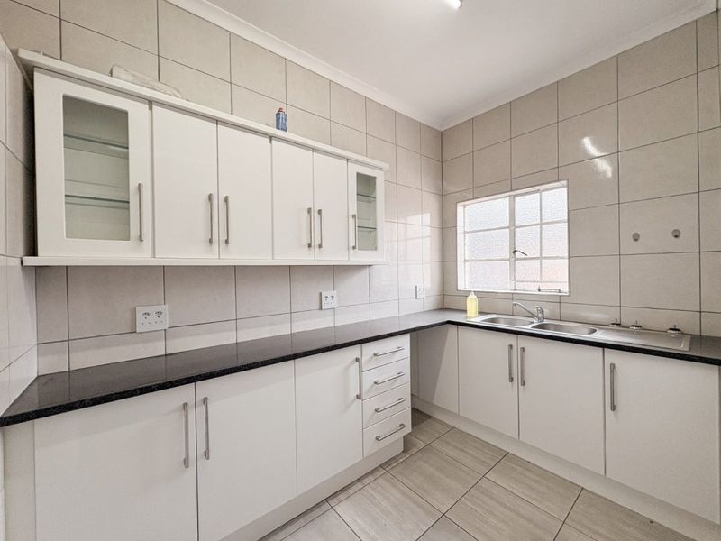 A clean, functional kitchen featuring white built-in cabinetry, dark laminate countertops, a double basin sink, and full-height wall tiling.