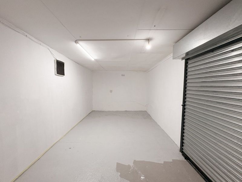 A clean, empty garage space featuring a secure roller shutter door, painted concrete flooring, and functional overhead lighting.