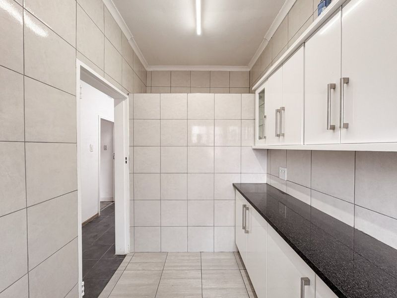 A clean, functional scullery area featuring tiled walls, granite countertops, and ample built-in cabinetry for storage and preparation.