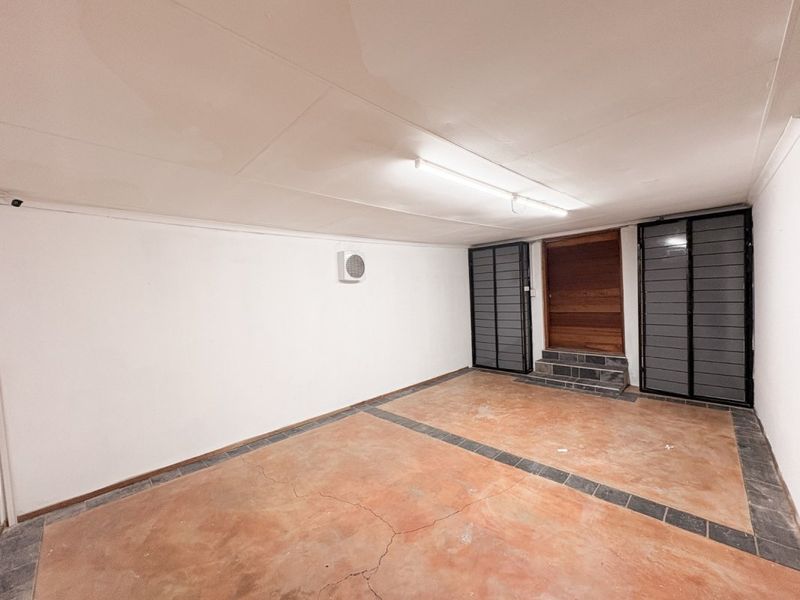 A clean, empty garage space featuring concrete flooring with decorative tile inlays, a timber entrance door, security gates, and integrated ventilation.