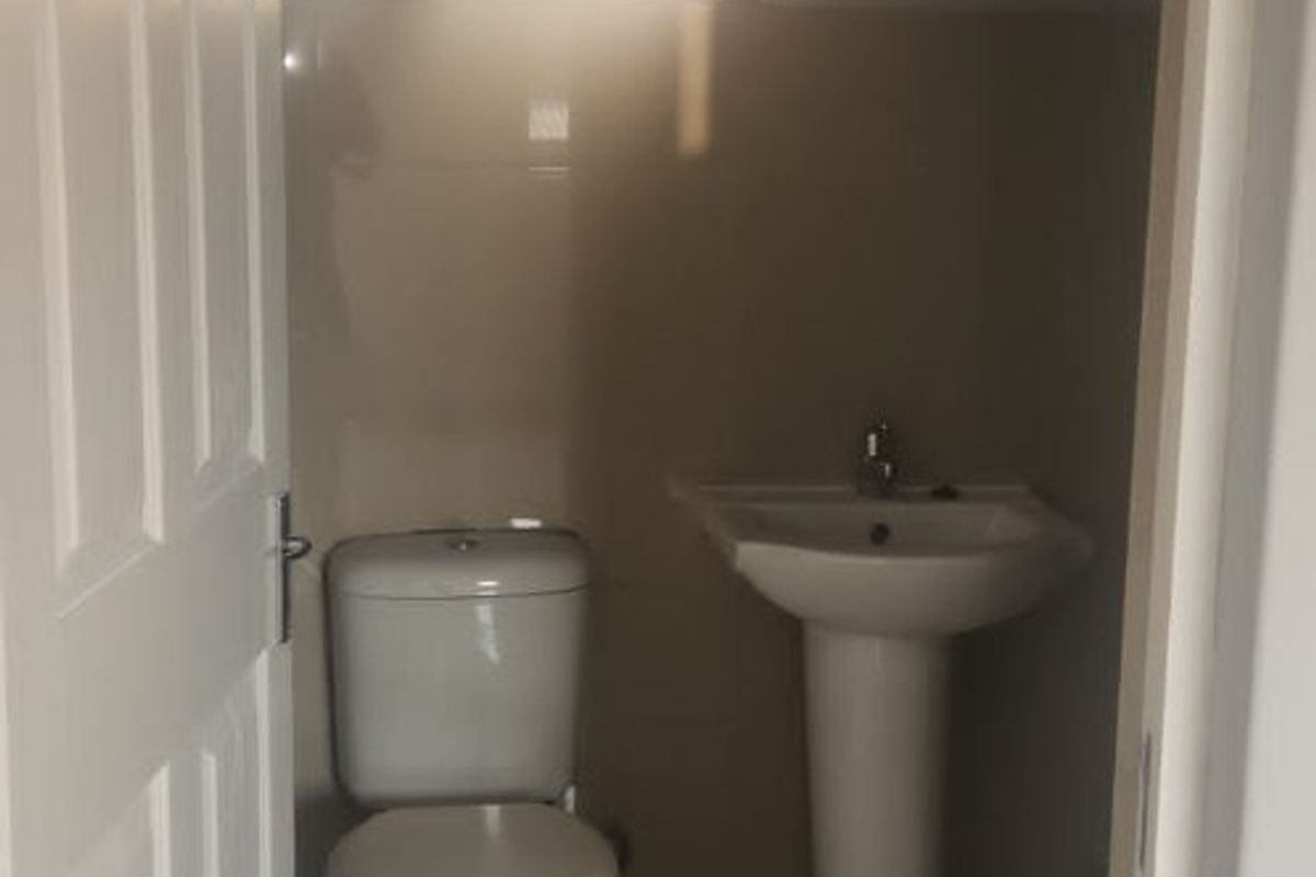 A compact bathroom featuring a pedestal washbasin, toilet, and neutral wall and floor tiling, providing a functional and clean space.
