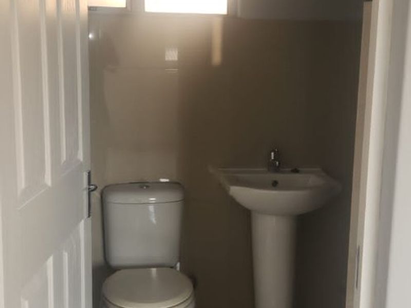 A compact bathroom featuring a pedestal washbasin, toilet, and neutral wall and floor tiling, providing a functional and clean space.