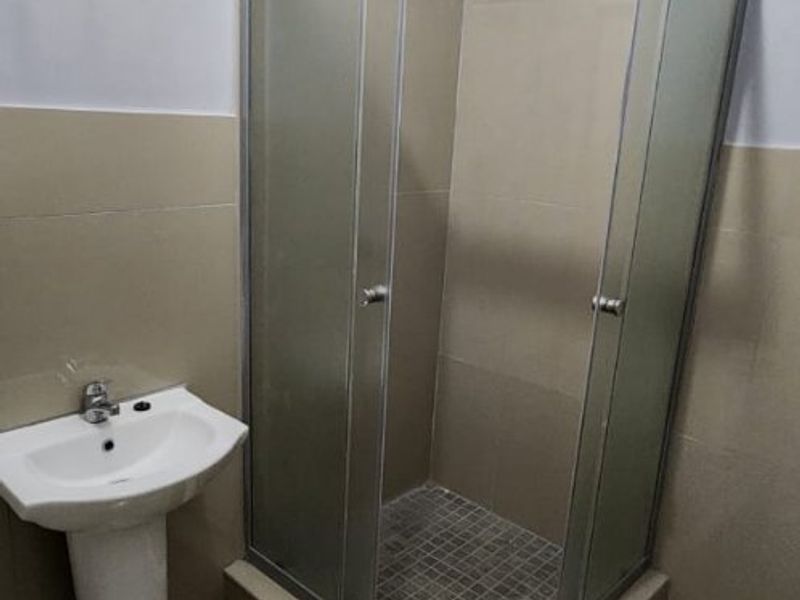 A clean bathroom featuring a pedestal basin and a corner shower enclosure with tiled walls and flooring.