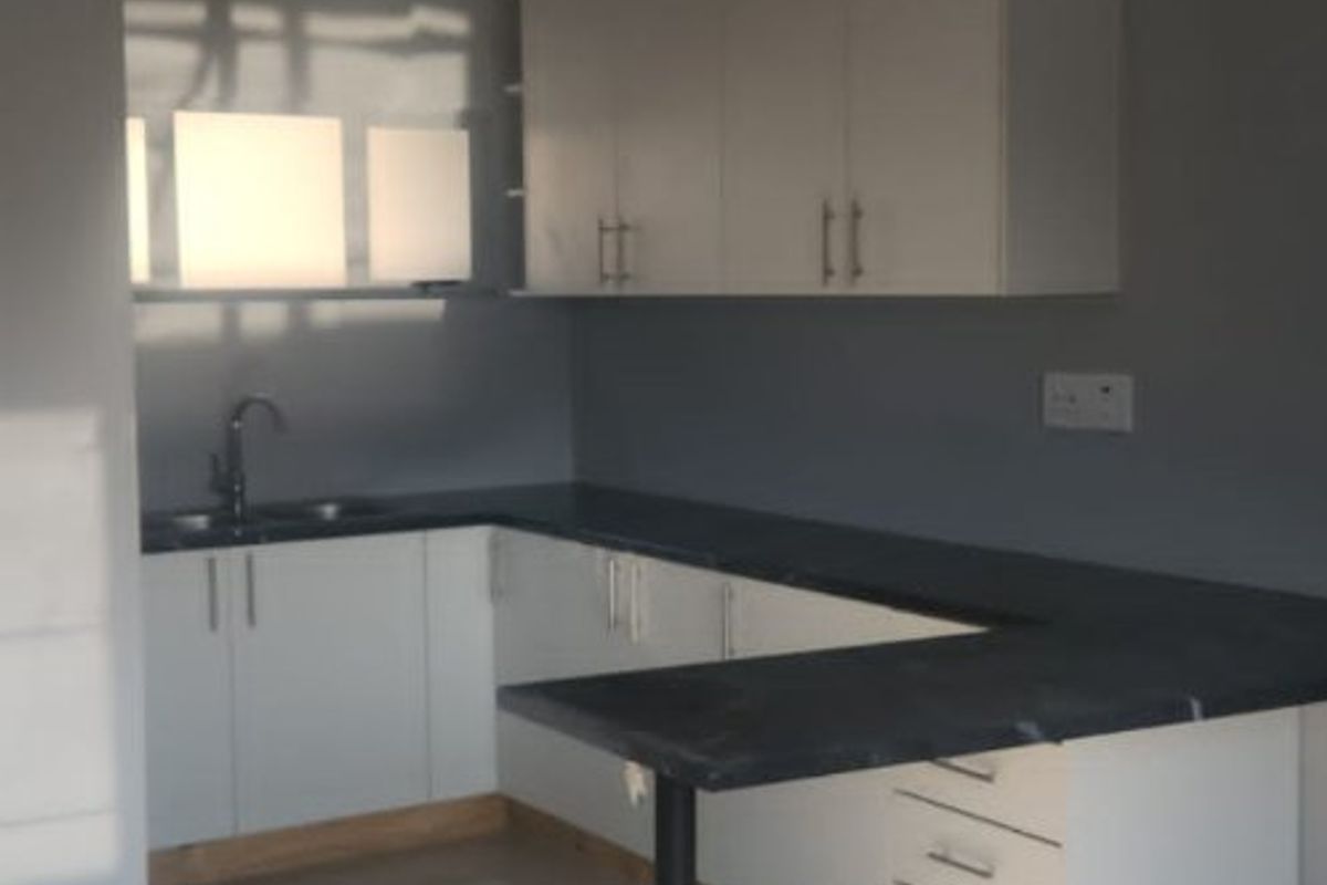 A clean, modern kitchen featuring white cabinetry, dark countertops, a breakfast bar, and tiled flooring, offering a bright and functional workspace.