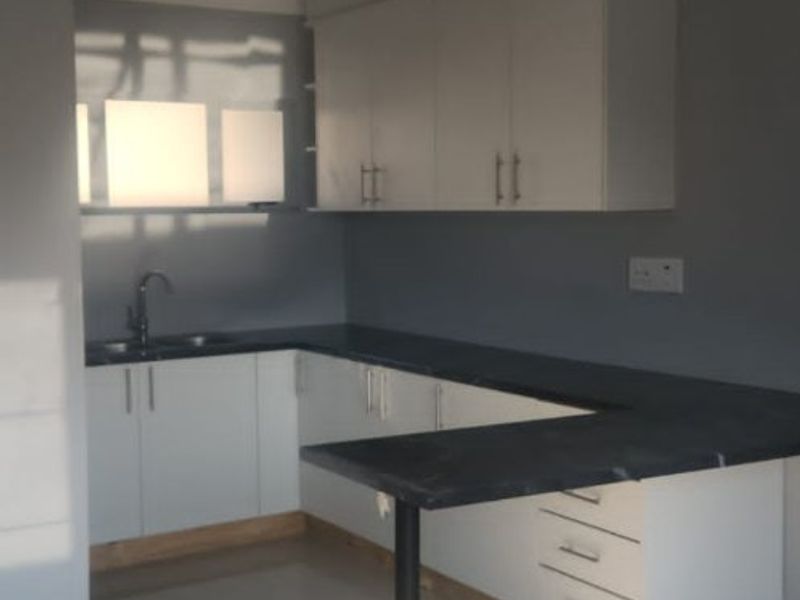 A clean, modern kitchen featuring white cabinetry, dark countertops, a breakfast bar, and tiled flooring, offering a bright and functional workspace.