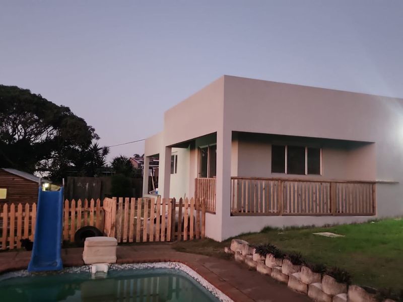 Rear exterior view of the property featuring a swimming pool, wooden fencing, and a raised deck area with modern rendered walls.