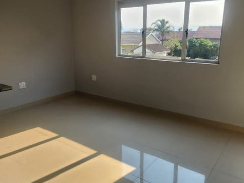 A bright, empty bedroom featuring neutral grey walls, large windows with natural light, and clean tiled flooring.
