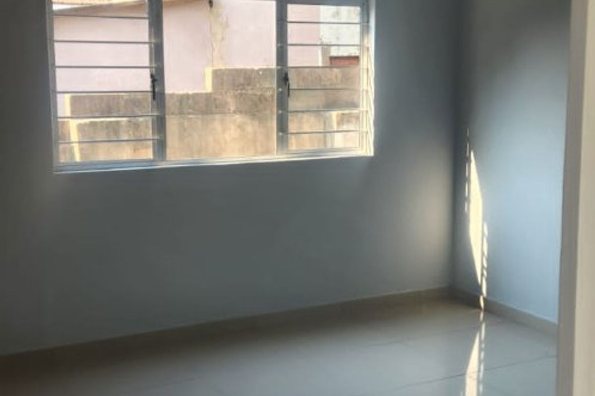 A bright, empty bedroom featuring polished tiled flooring, neutral wall paint, and a window fitted with security bars.