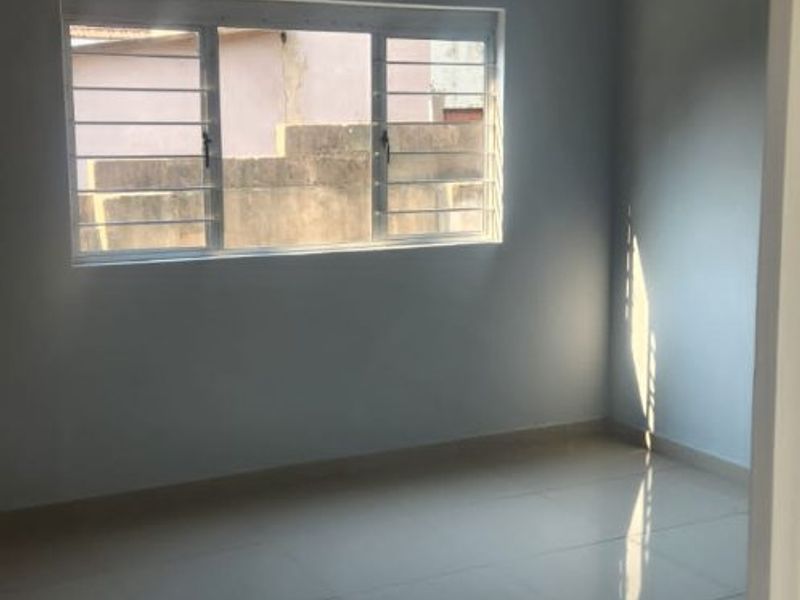 A bright, empty bedroom featuring polished tiled flooring, neutral wall paint, and a window fitted with security bars.