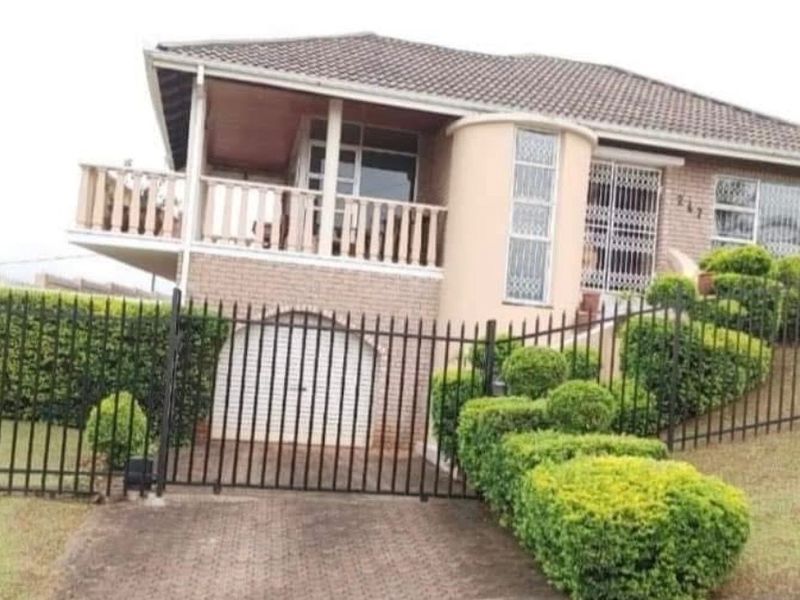 Front elevation of a multi-level brick house featuring a balcony, paved driveway, secure garage, and landscaped garden with perimeter fencing.
