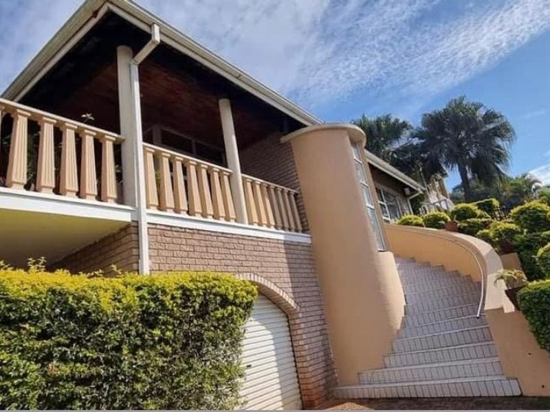 Front elevation of a multi-level house featuring a curved staircase, upper balcony with balustrade, brick exterior, and integrated garage.