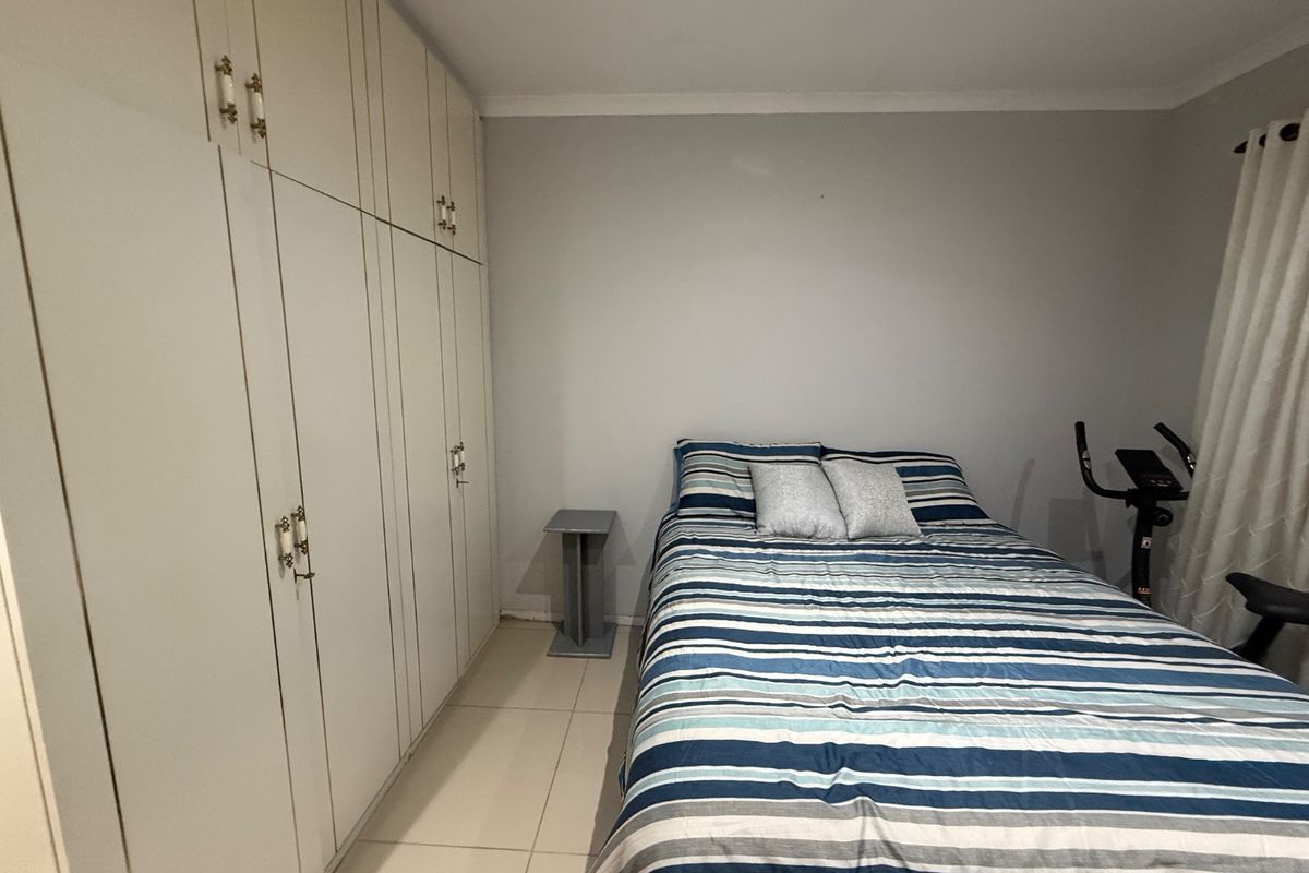 A functional bedroom featuring neutral tiled flooring and extensive built-in cupboard storage with classic hardware.
