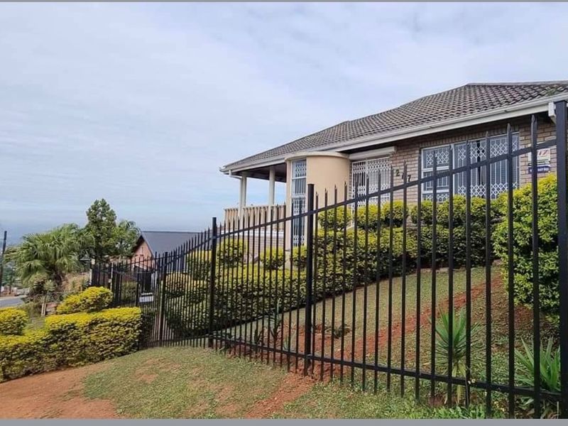 Front exterior view of a brick house featuring a tiled roof, covered patio, and secure metal perimeter fencing.