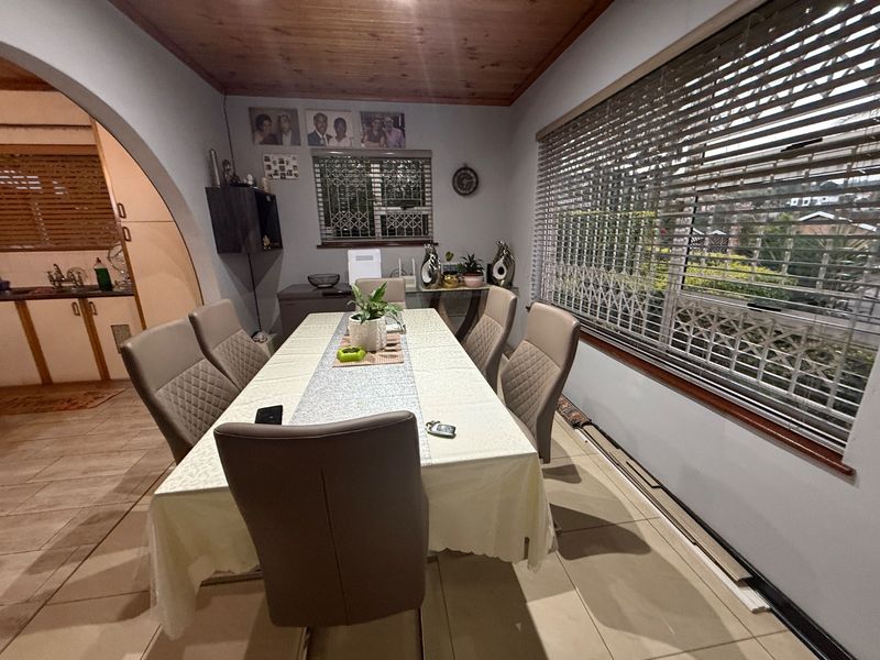 Dining room featuring tiled flooring, a timber ceiling, and large windows fitted with security shutters, providing a functional space for family meals.