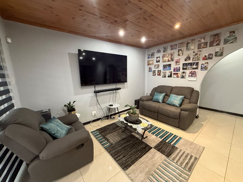 A comfortable living room featuring tiled flooring, a warm timber tongue and groove ceiling with recessed lighting, and a distinct arched entryway.
