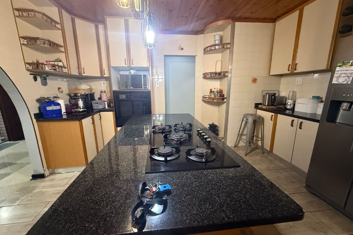 Spacious kitchen featuring a large granite-topped island with a built-in gas hob, timber ceiling, and ample built-in cabinetry.