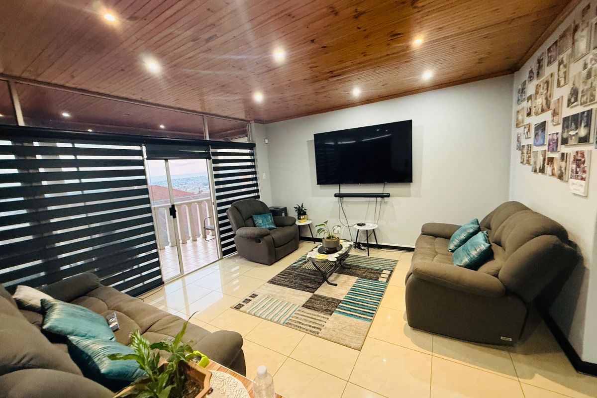 Spacious living room featuring a warm timber ceiling, recessed lighting, large format floor tiles, and sliding glass doors leading to an outdoor balcony area.
