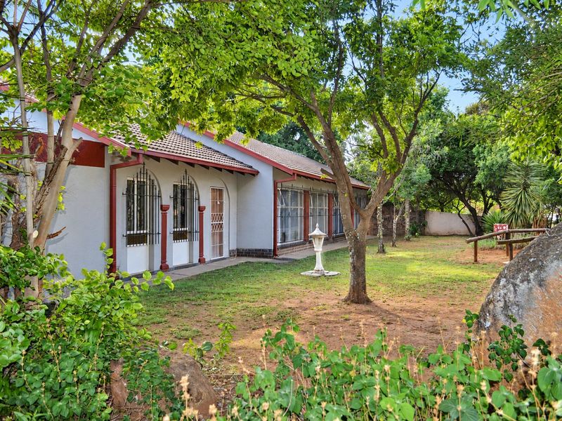 Rear view of the house featuring a tiled roof, security bars on windows, and a spacious garden area with mature trees.
