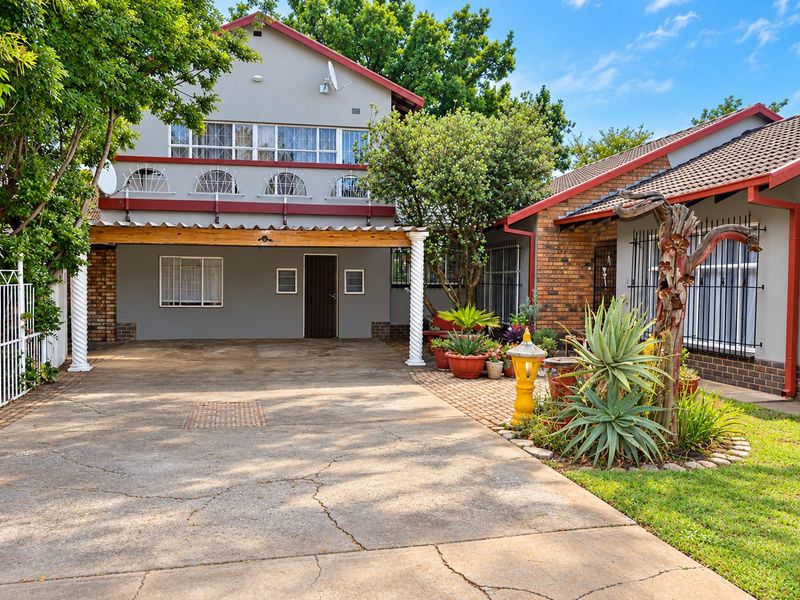 Front view of a multi-level house featuring a concrete driveway, covered carport, and brick and rendered exterior walls with security bars on windows.