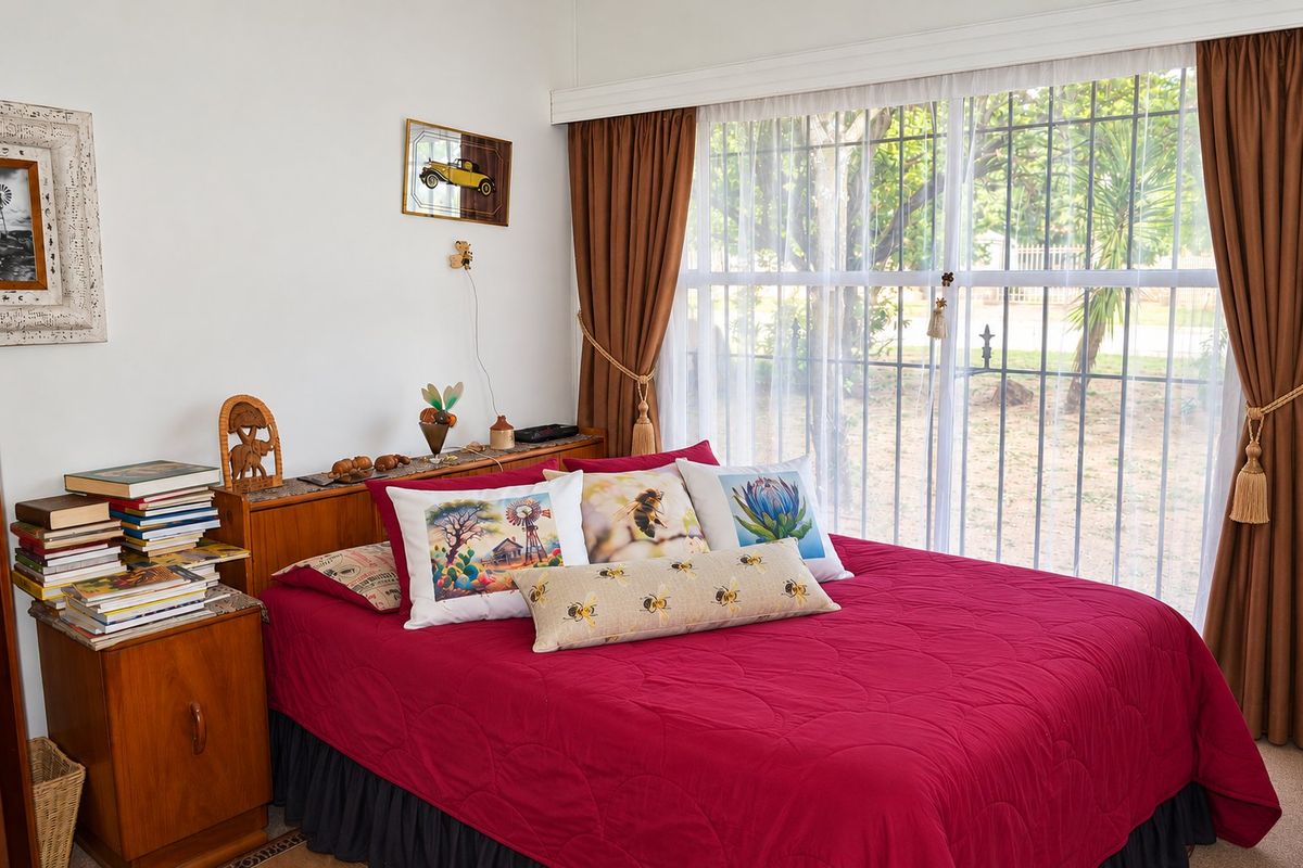 A bedroom featuring large windows with security bars and neutral wall finishes, providing a functional space with natural light.
