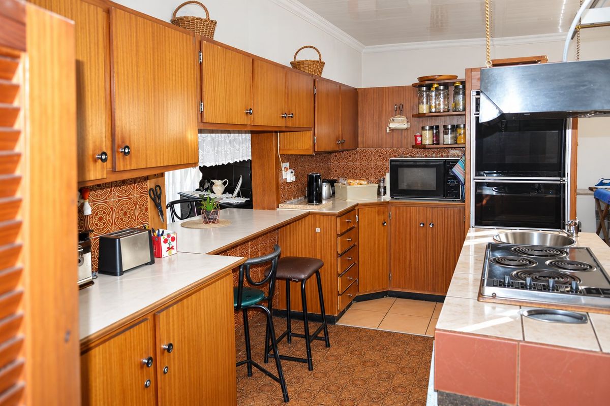A dated kitchen featuring extensive wooden cabinetry, tiled splashbacks, built-in oven, and an electric hob set into a tiled island counter.