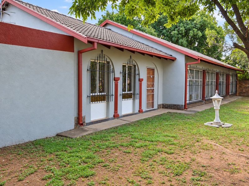Rear exterior view of the house featuring a tiled roof, security bars on windows, and a concrete pathway leading along the building facade.