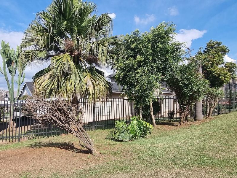 A well-maintained garden area featuring mature trees and secure metal perimeter fencing, providing a pleasant outdoor space.