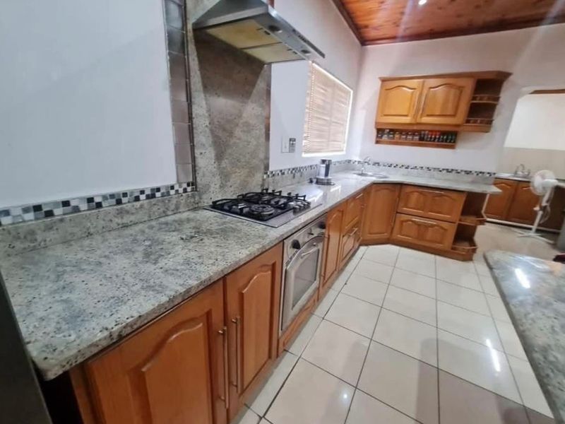 A functional kitchen featuring granite countertops, wooden cabinetry, built-in oven, gas hob, and tiled flooring with a timber ceiling finish.