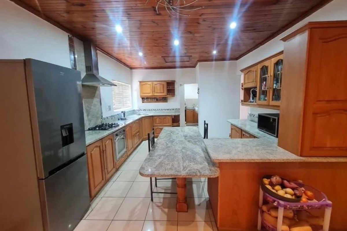 Spacious kitchen featuring wooden ceiling, granite countertops, built-in wooden cabinetry, gas hob, extractor fan, and tiled flooring.