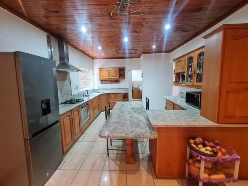 Spacious kitchen featuring wooden ceiling, granite countertops, built-in wooden cabinetry, gas hob, extractor fan, and tiled flooring.