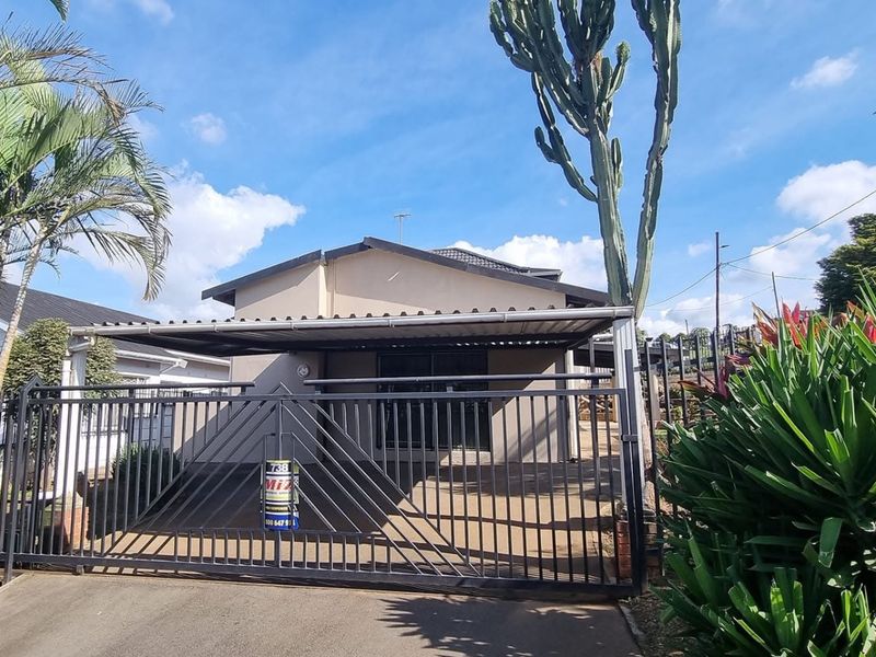 Front view of a residential property featuring a paved driveway, a metal sliding gate, and a covered carport area.