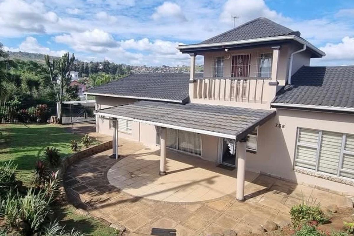 Rear view of a two-story house featuring a covered patio, paved courtyard, upper-level balcony, and landscaped garden area.